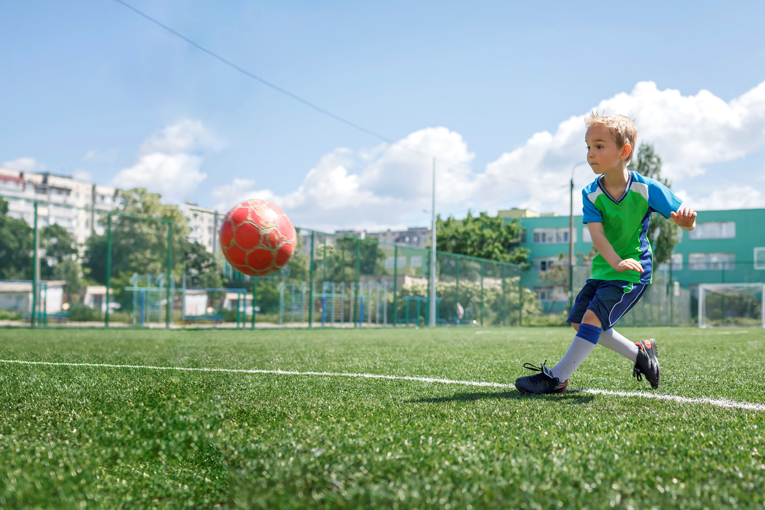 little-boy-in-blue-and-green-form-playing-football-on-open-field-in-the-yard-a-young-soccer-player.jpg