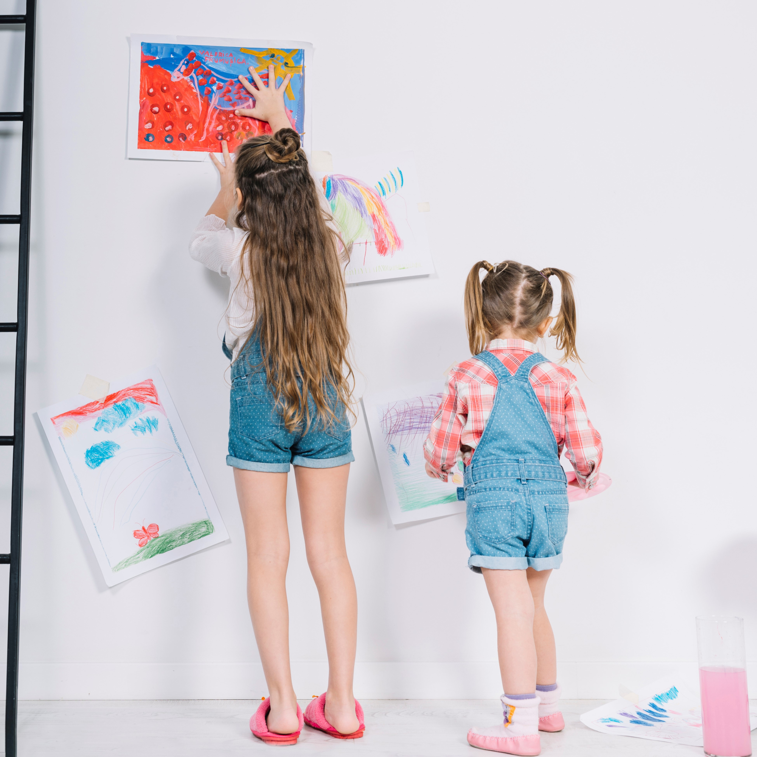 2 little-girls-hanging-drawings-on-white-wall.jpg